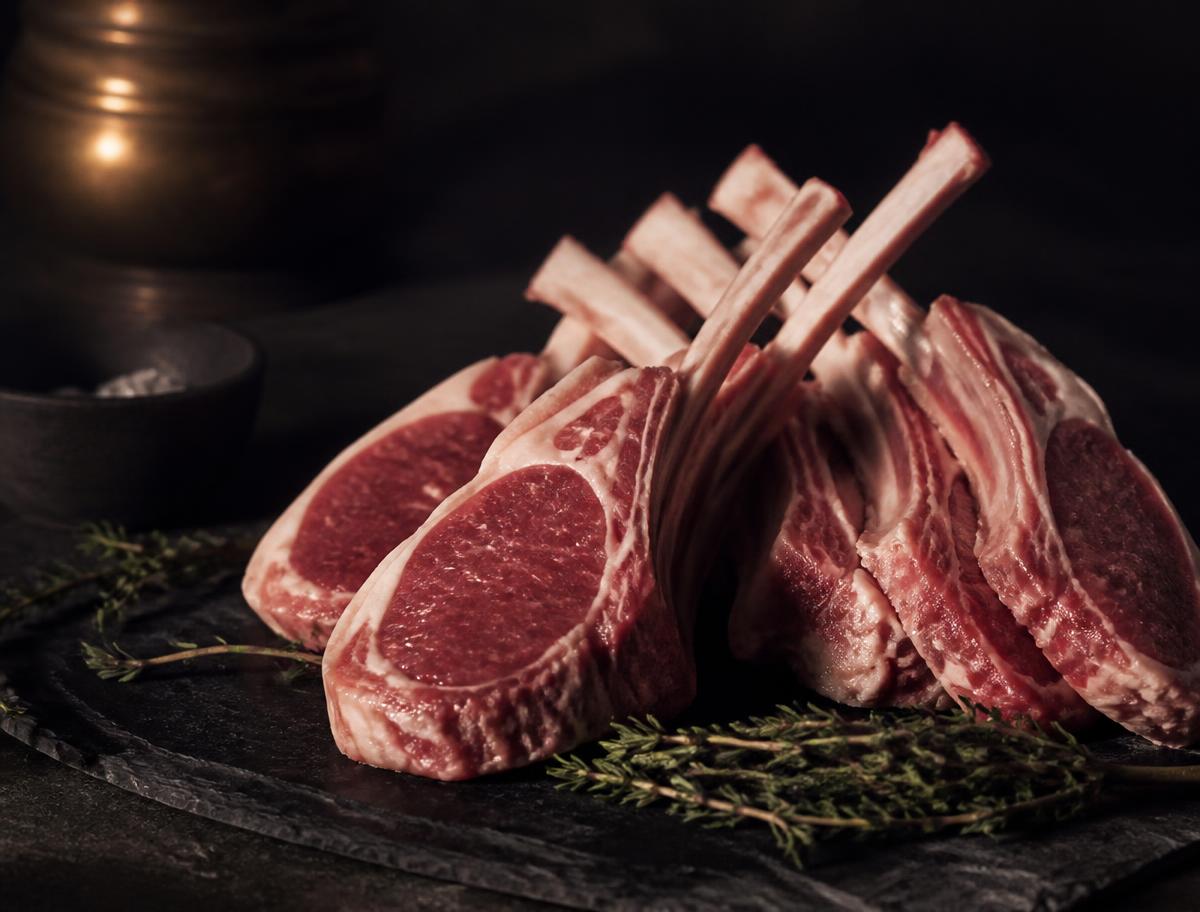 A frenched rack of organic lamb cutlets on dark slate with fresh thyme